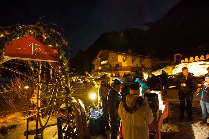 Advent window number 18 with fairy lights, guests and locals with punch in front of an illuminated house
