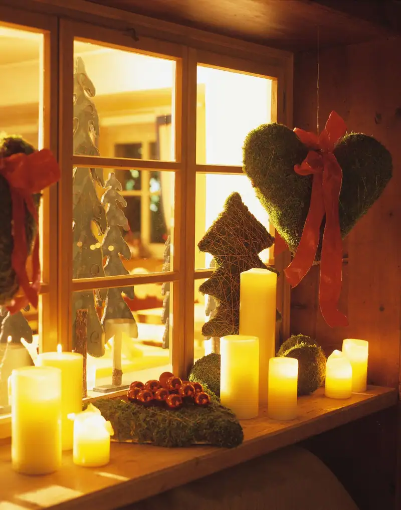 Window decorated for Advent with candles, a moss heart and a red bow