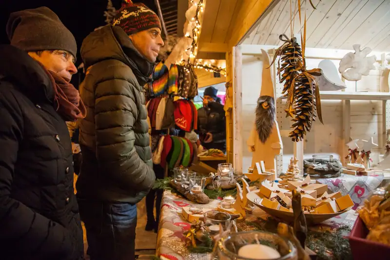 Couple at an Advent market stall with wooden stars, lanterns, cones and knitted hats