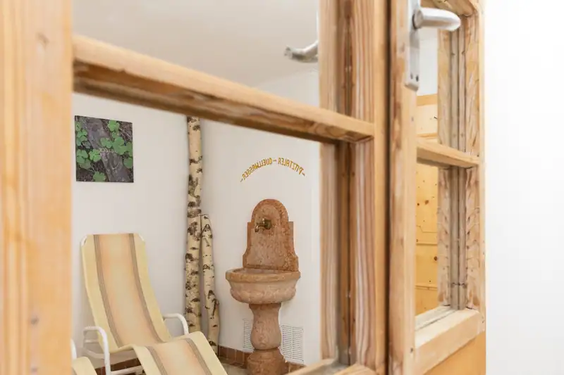 Blick durch ein Holzfenster in den Ruheraum mit Brunnen