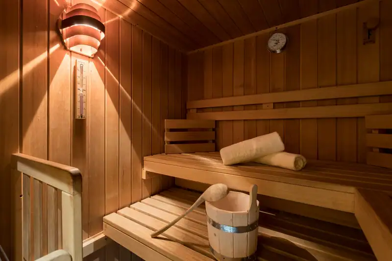 Sauna aus hellem Holz mit Aufgusskübel und gerollten Handtüchern