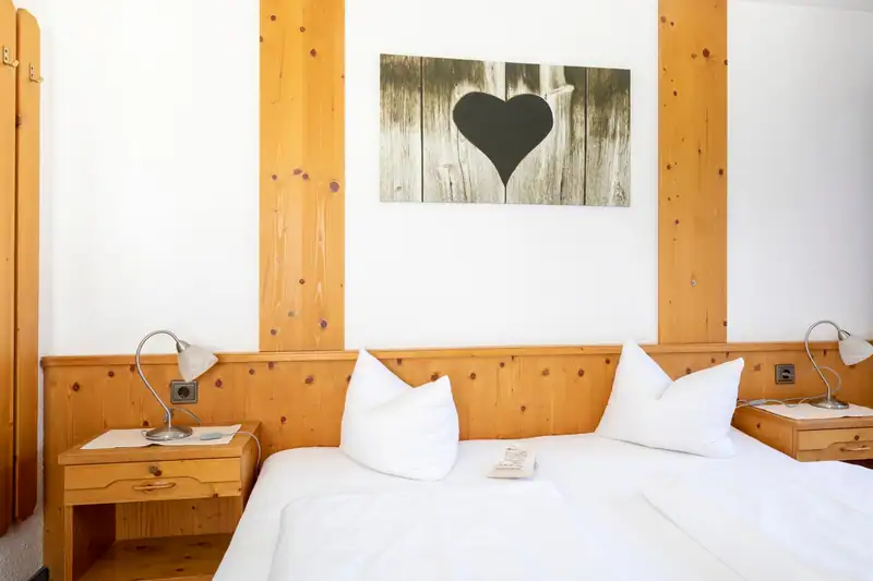 Doppelbett vor Holzvertäfelung mit Nachttischlampen und Herz-Bild