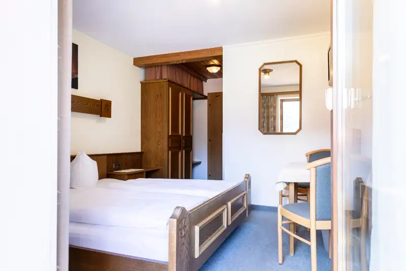 Doppelzimmer mit Holzbett, Kleiderschrank, Spiegel und Tisch mit zwei Stühlen
