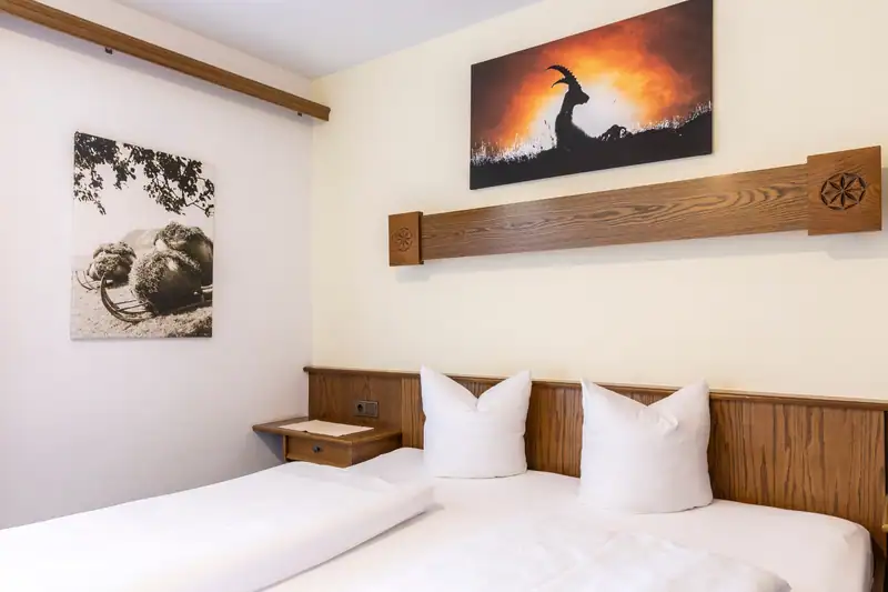 Doppelbett mit dunkler Holzvertäfelung unter einem Wandbild mit Steinbock im Abendlicht