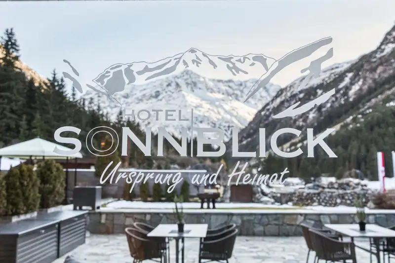 Window pane with hotel logo and the words “Ursprung und Heimat” in front of snowy mountains