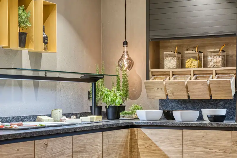 Breakfast buffet with herb pots, cheese, white bowls and muesli drawers under a glass display