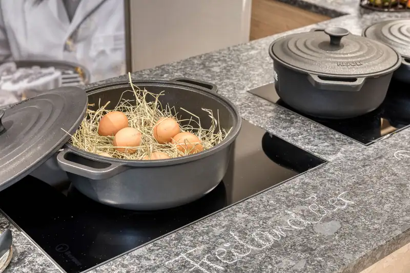 Fresh eggs in hay in an open pot on the hob, with the chalk lettering “Freilandeier” (free-range eggs) on the granite