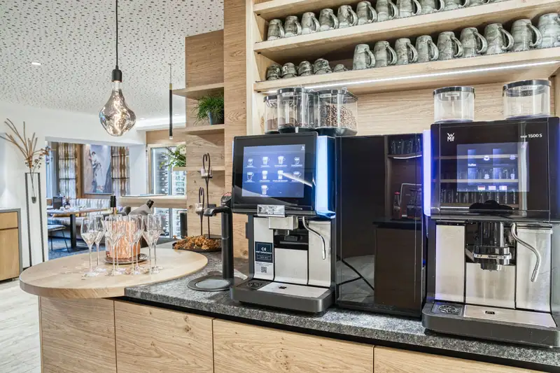 Coffee station with two fully automatic coffee machines, a cup shelf and sparkling wine glasses on a round wooden counter