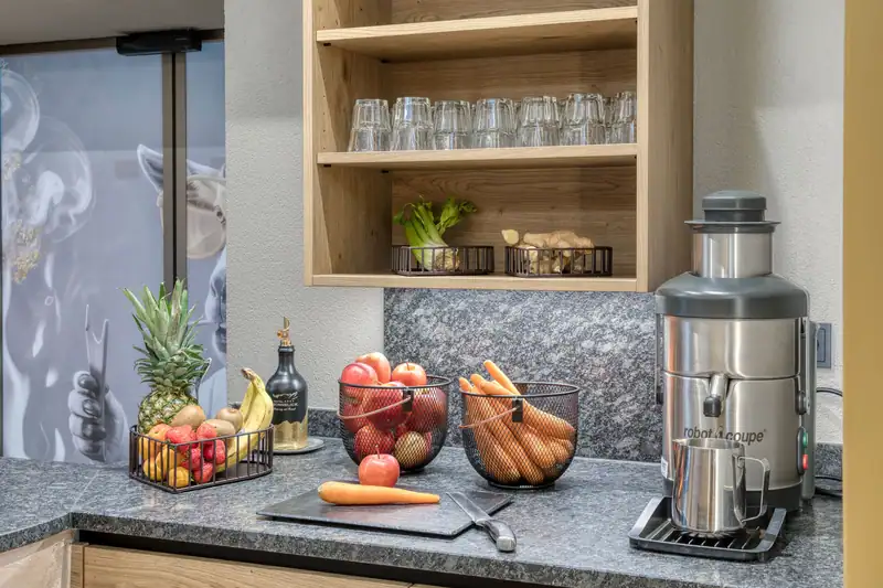 Fruit, carrots and glasses on the wooden shelf next to the juicer