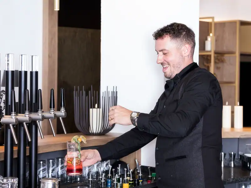 Bartender serving a red long drink with physalis at the tap
