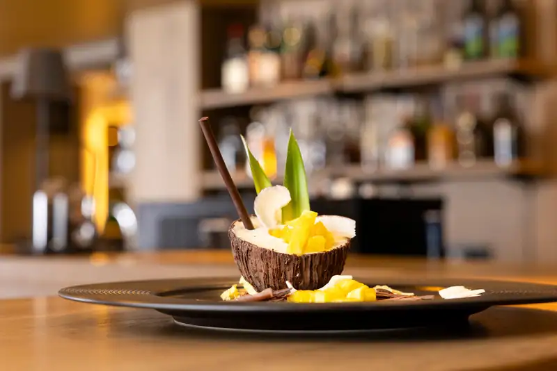 Dessert in a chocolate-coconut shell with pineapple, in front of the bar