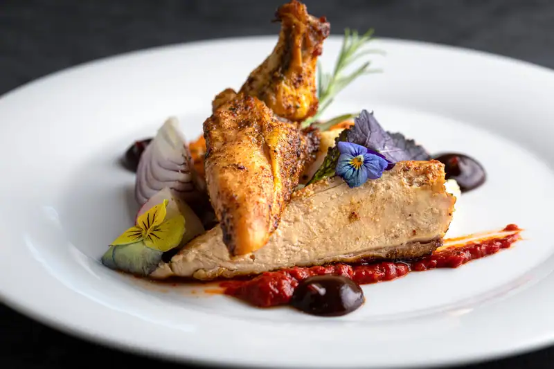 Roast chicken with vegetables, pepper sauce and edible flowers on a white plate