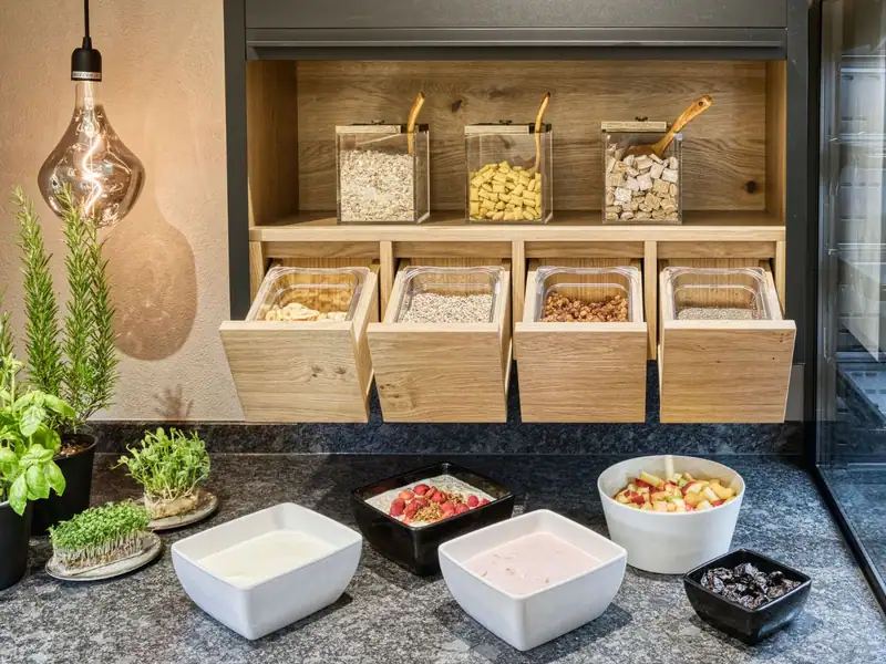 Muesli station with cereals in wooden drawers, yoghurt, fruit salad and fresh herbs