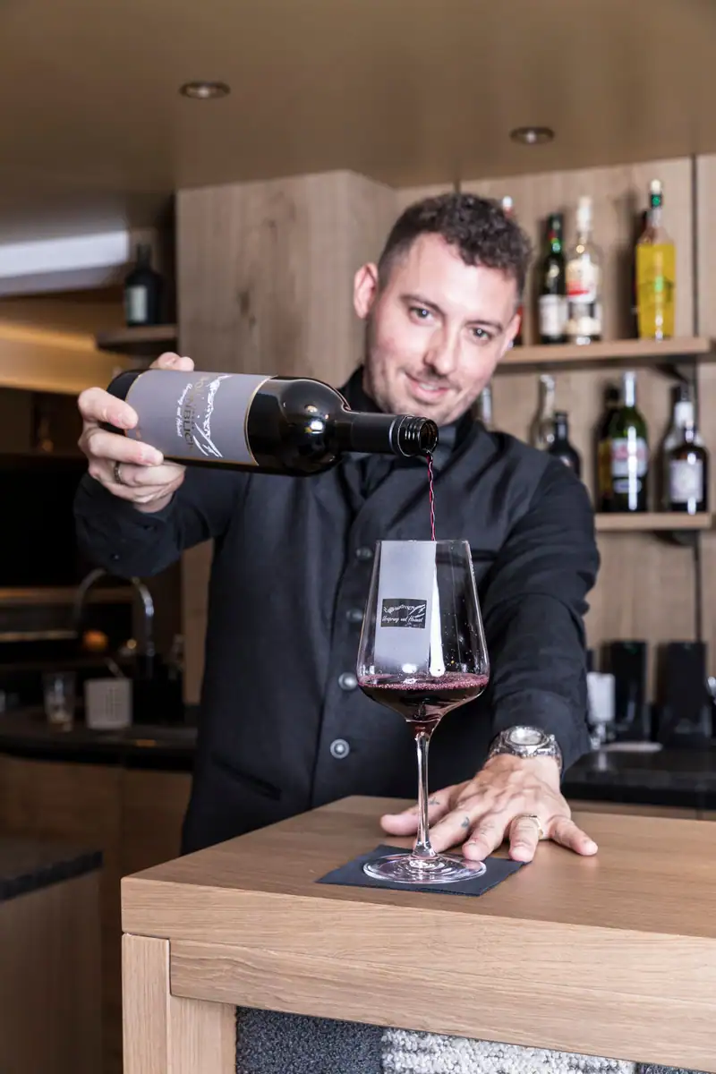 Bartender pouring red wine with a Sonnblick label into a glass
