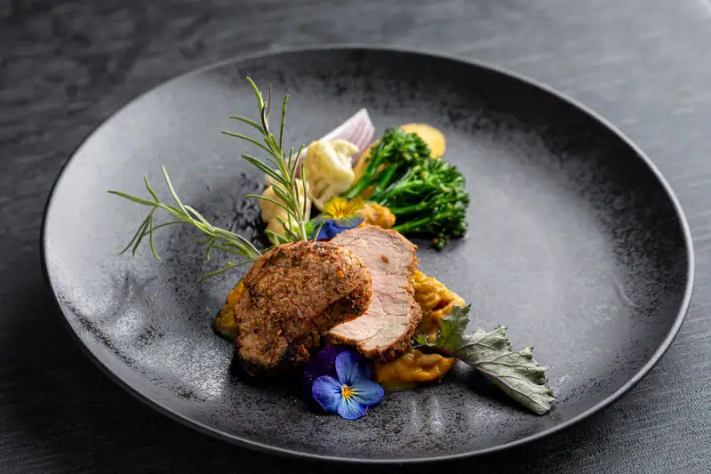 Pork fillet with broccoli, cauliflower and pumpkin purée on a dark plate