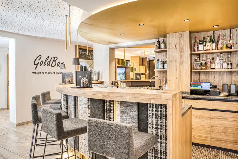 The new GoldBar with round wooden counter, grey bar stools and the lettering “wo jeder Moment glänzt!” (where every moment shines)