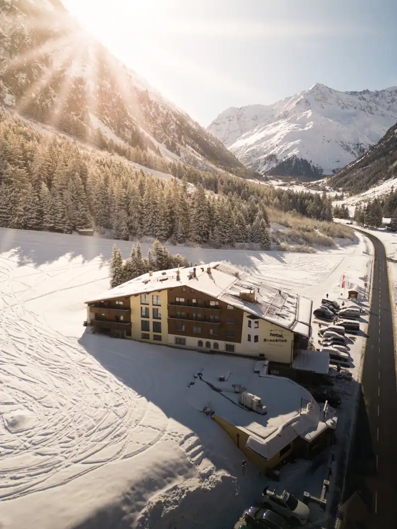 The hotel in the snowy valley from above, with road and car park beside it