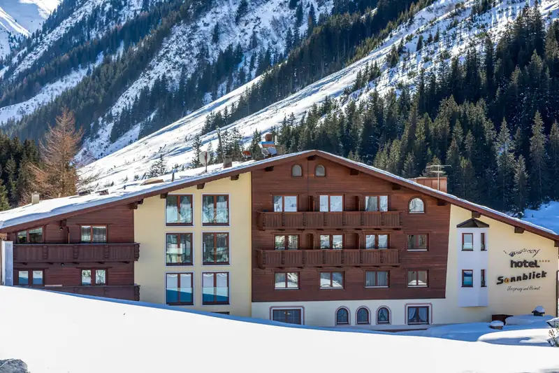 Hotel facade with wooden balconies and Sonnblick lettering in front of snowy mountainsides