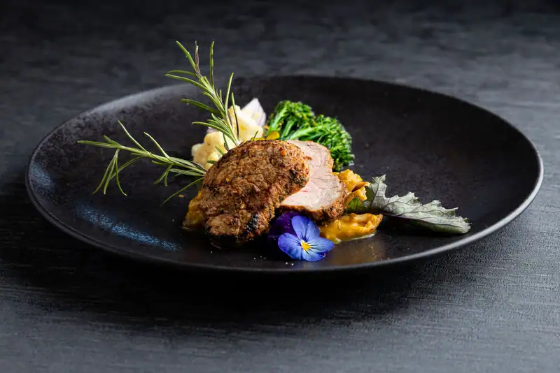 Roast fillet with rosemary, broccolini, cauliflower, pumpkin purée and horned violets on a black plate