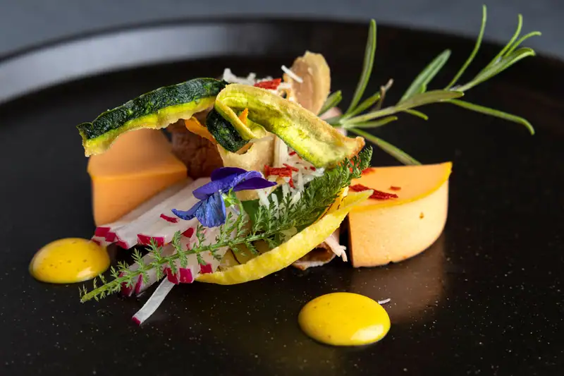 Terrine with vegetable chips, radish strips, yarrow and violets with dots of yellow sauce