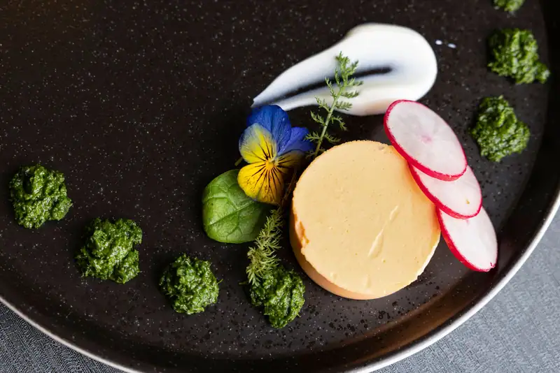 Terrine with radish slices, herb pesto, white cream and pansies on a black plate