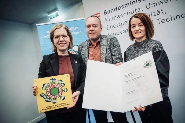 Presentation of the certificate and Ecolabel plaque to Hotel Sonnblick in front of a wall of the Federal Ministry