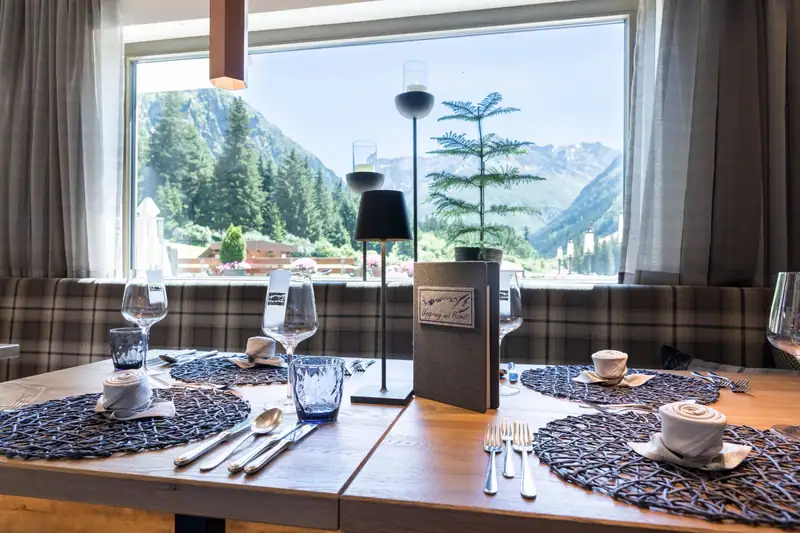 Laid table at the panoramic window with a view over forest and mountains to the head of the valley