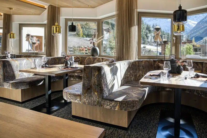 Restaurant with velvet-upholstered booths, golden pendant lights and windows overlooking snowy mountains