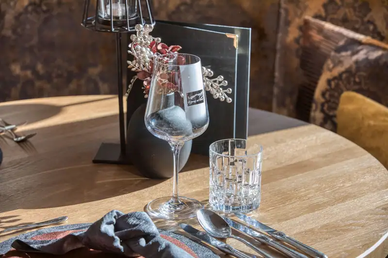 Wine glass with Sonnblick logo, water glass, cutlery and menu on a sunlit wooden table