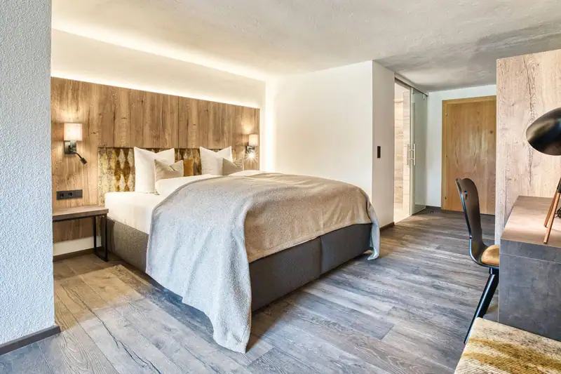 Box-spring bed with reading lamps in front of the oak wall, the desk on the right