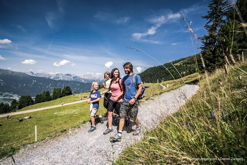 Family with two children on an alpine path on the Hochzeiger, grazing cows and mountains in the background