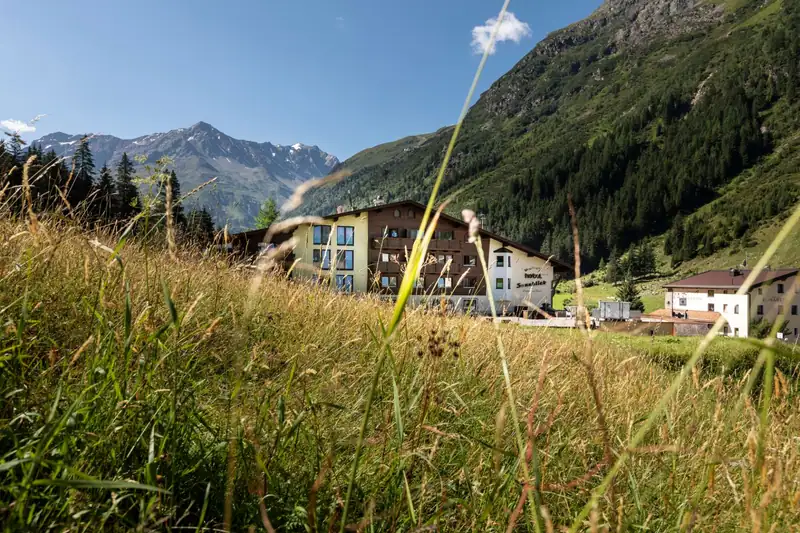Hotel Sonnblick behind the tall grasses of a mountain meadow, peaks in the background