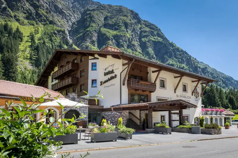 Entrance of Hotel Sonnblick with canopy and flower boxes in front of a green mountainside