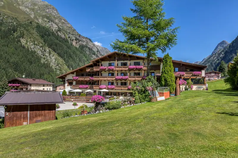 GenussHotel Sonnblick with flower-decked wooden balconies behind a large larch and lawn in summer