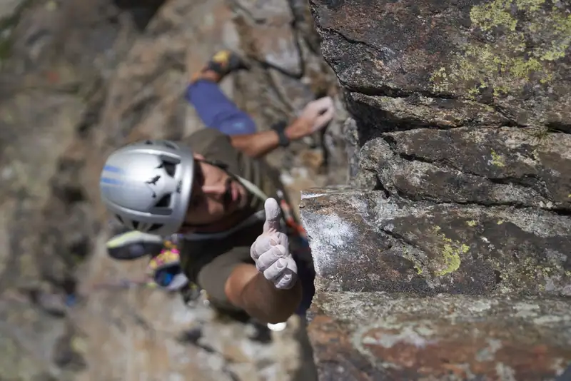 Climber with helmet reaching for a rock edge from below, view from above