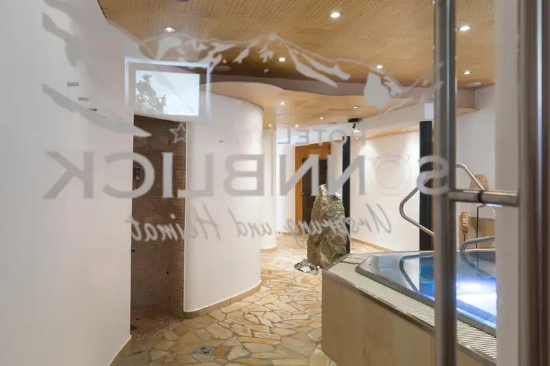 View through the glass door with Sonnblick logo into the spa area with whirlpool and natural stone floor