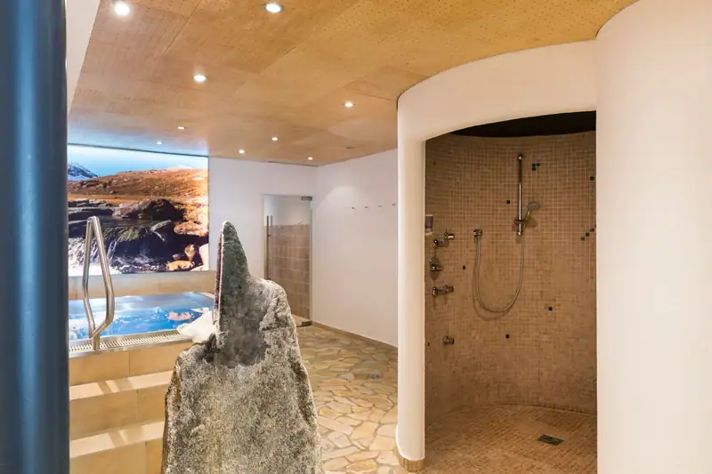 Round experience shower with mosaic tiles, an amethyst stone and the whirlpool in front