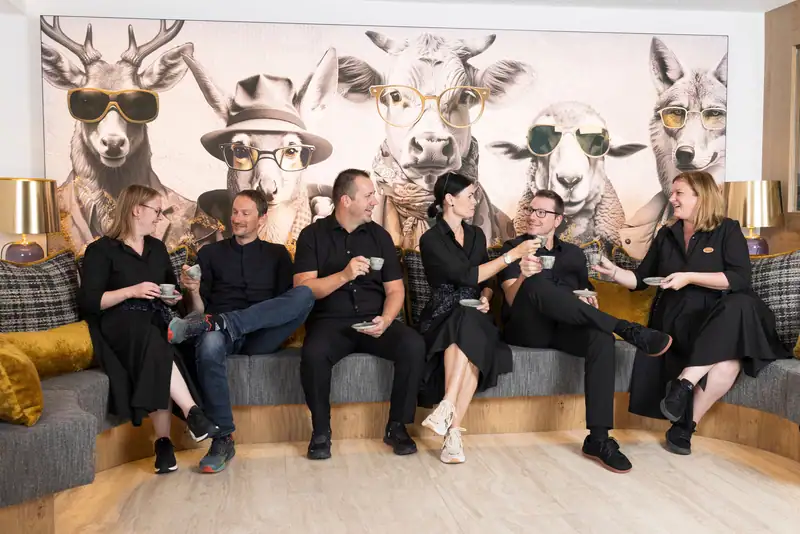 The GenussHotel Sonnblick team having coffee on the lounge bench in front of the animal mural