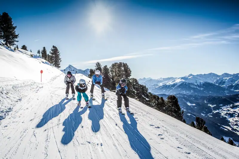Family with two children on skis on a sunny piste, the Inn valley in the background