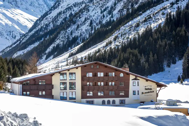 Hotel Sonnblick with wooden balconies in front of snowy, wooded mountainsides