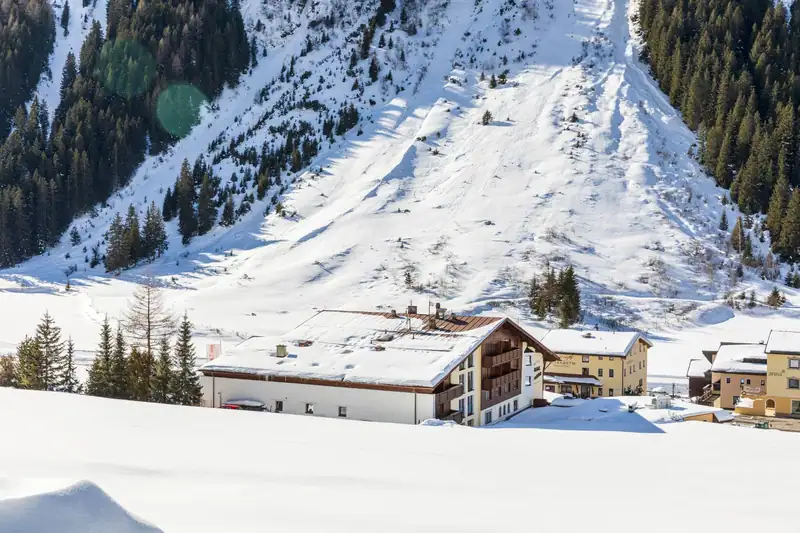 The hotel in the snow at the foot of a steep, snowy mountainside