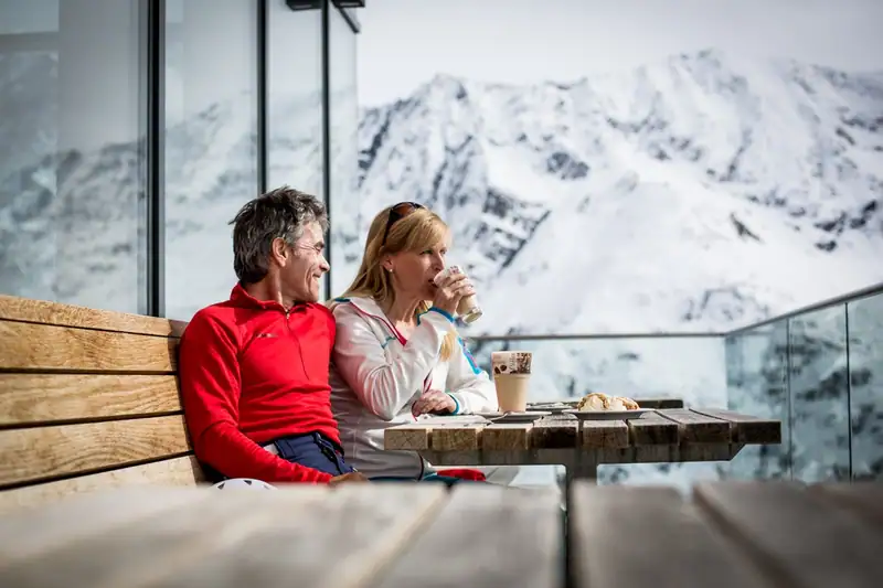 Couple with coffee and cake on the sun terrace in front of snow-covered mountains
