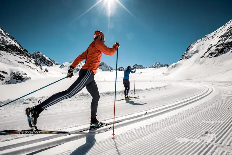 Two cross-country skiers using the classic technique on the glacier trail in bright sunshine