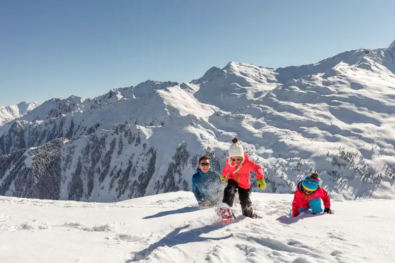 Father with two children snowshoeing in deep snow in front of a mountain panorama