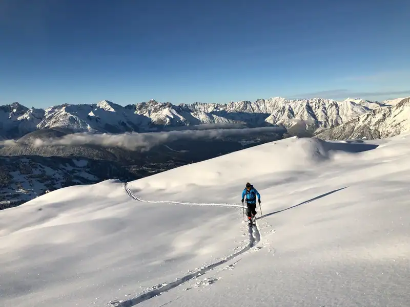 Ski tourer climbing in powder snow, a sea of clouds and mountain range behind