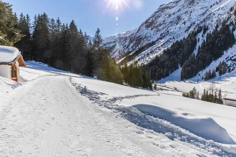 Groomed winter path by a small chapel, sunny snowy mountains behind