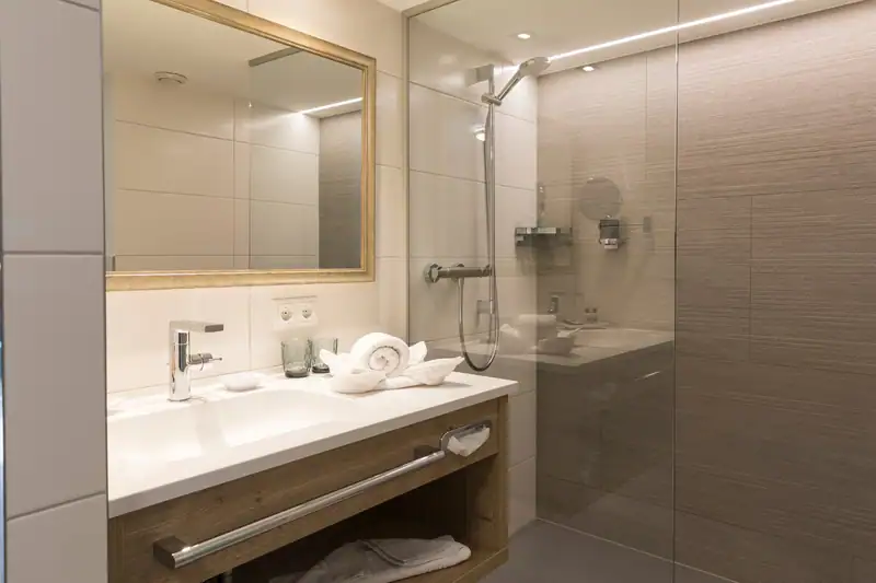 Bathroom with wooden washbasin, gold-framed mirror and shower with glass wall