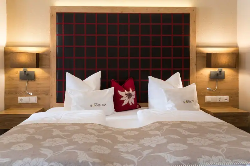 Double bed from the front with red-checked headboard, reading lamps and edelweiss cushions