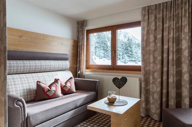 Pull-out sofa bed with heart cushion and side table by the window with a view of snow-covered trees