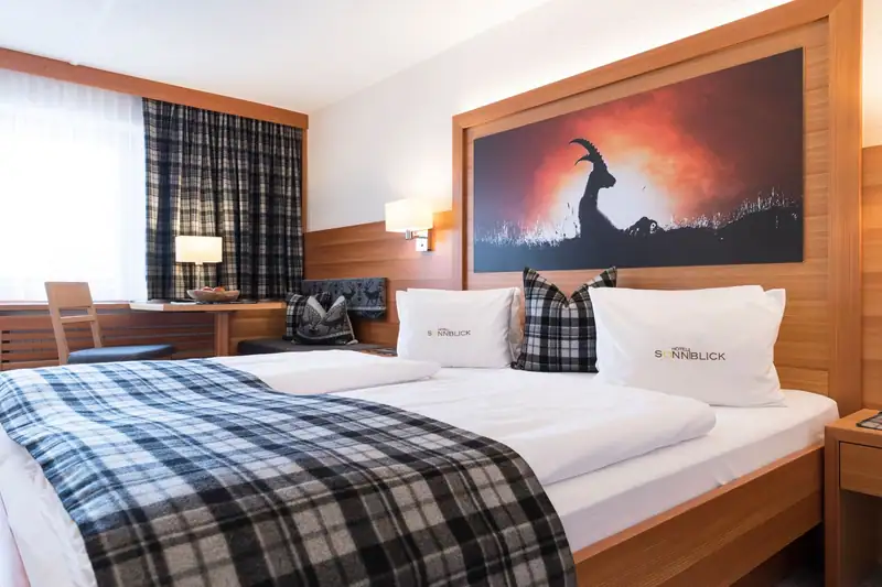 Double bed with checked blanket and cushions with the Sonnblick logo